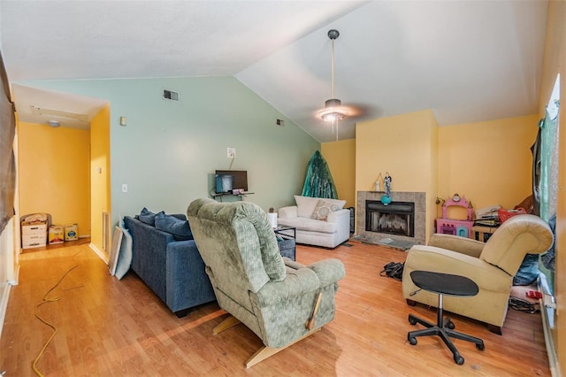 living room featuring a tiled fireplace, lofted ceiling, and light hardwood / wood-style flooring