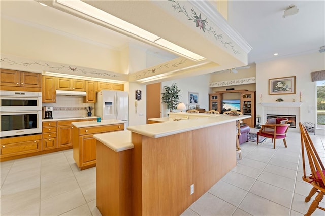 kitchen featuring crown molding, white appliances, an island with sink, light tile patterned flooring, and decorative backsplash