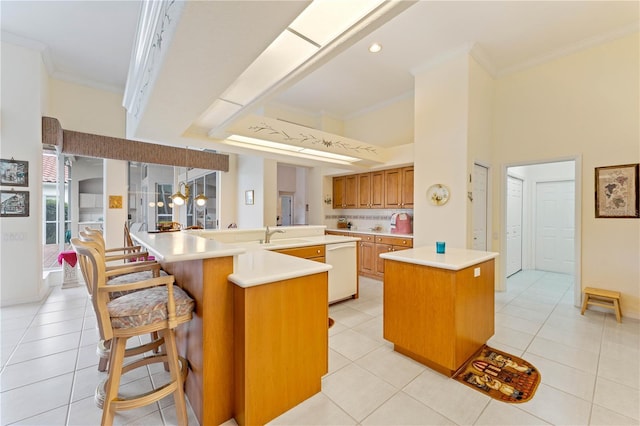 kitchen with light tile patterned floors, crown molding, a kitchen breakfast bar, and an island with sink