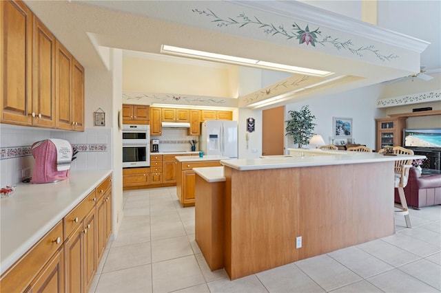 kitchen with white appliances, a center island, tasteful backsplash, a kitchen bar, and light tile patterned flooring