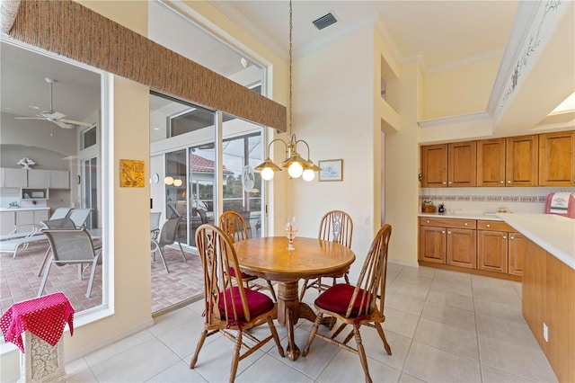 dining room featuring a towering ceiling, ornamental molding, ceiling fan with notable chandelier, and light tile patterned floors