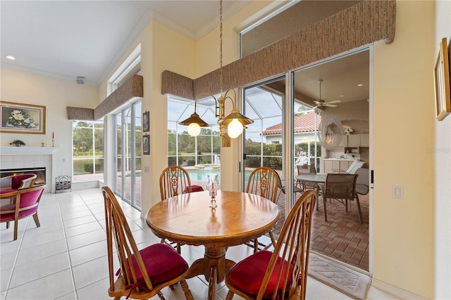 dining room with a tiled fireplace, light tile patterned floors, ornamental molding, and ceiling fan