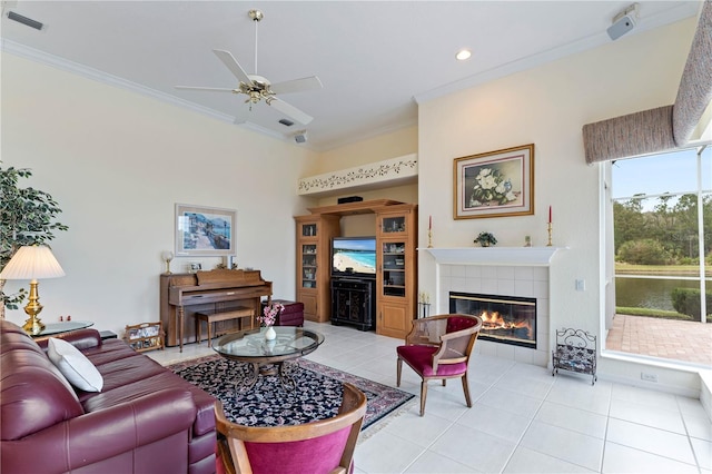 tiled living room with ceiling fan, ornamental molding, and a tile fireplace