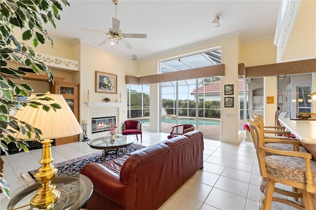 living room featuring light tile patterned flooring, crown molding, a towering ceiling, ceiling fan, and a tiled fireplace