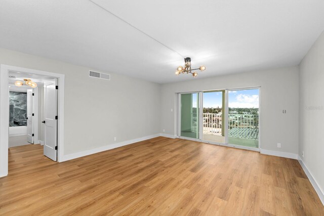 spare room featuring light wood finished floors, baseboards, visible vents, and a chandelier