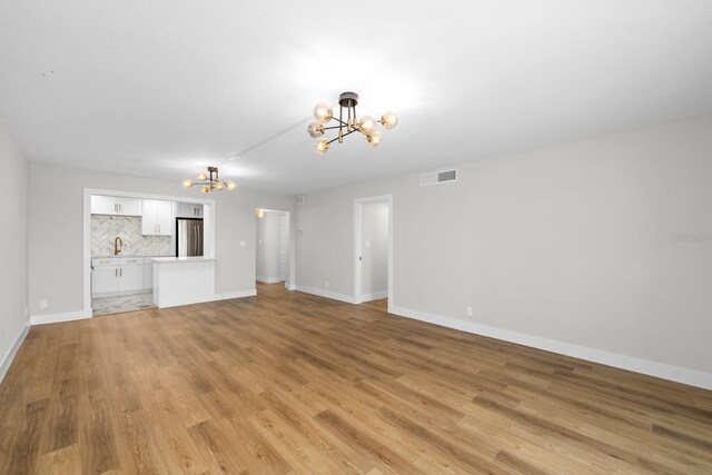 unfurnished living room with baseboards, visible vents, light wood finished floors, and an inviting chandelier