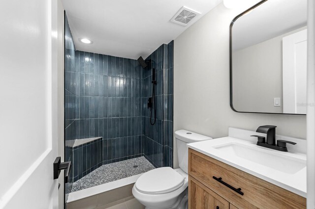 full bathroom with toilet, visible vents, a tile shower, and vanity