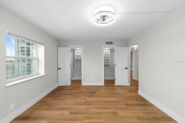 unfurnished bedroom featuring light wood-style flooring, a walk in closet, visible vents, and baseboards