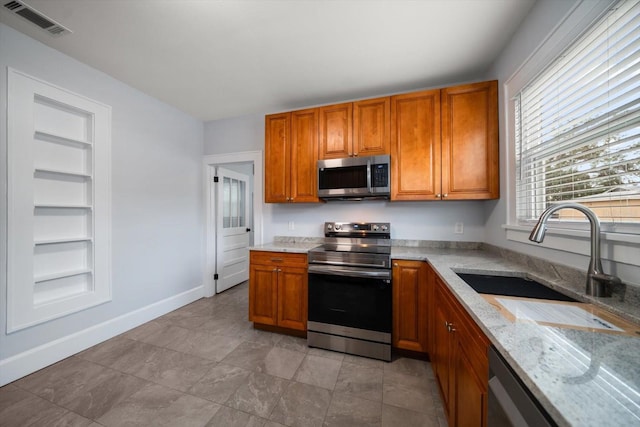 kitchen featuring light stone countertops, built in shelves, appliances with stainless steel finishes, and sink