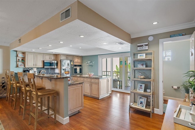 kitchen with light hardwood / wood-style floors, a breakfast bar area, stainless steel appliances, dark stone countertops, and a kitchen island