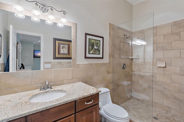 bathroom with toilet, a tile shower, tile walls, crown molding, and vanity