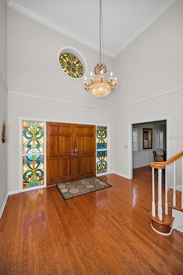 entrance foyer with crown molding, a towering ceiling, a notable chandelier, and hardwood / wood-style flooring