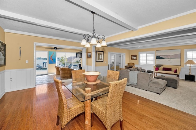 dining space featuring ceiling fan with notable chandelier, a wealth of natural light, beam ceiling, and hardwood / wood-style flooring