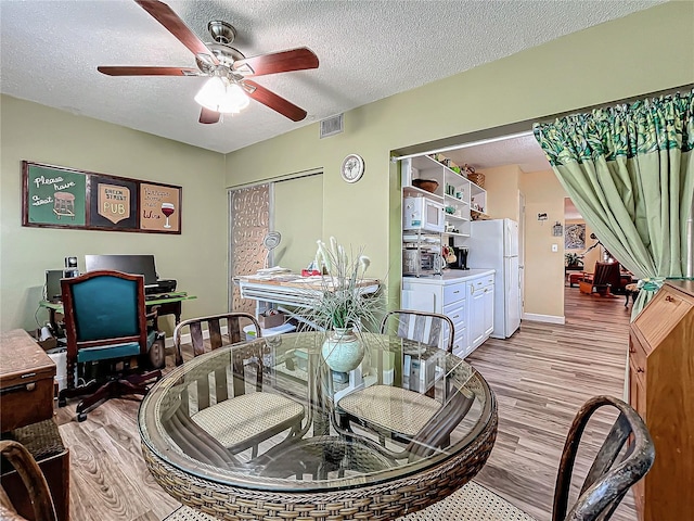 dining space with ceiling fan, a textured ceiling, and light wood-type flooring