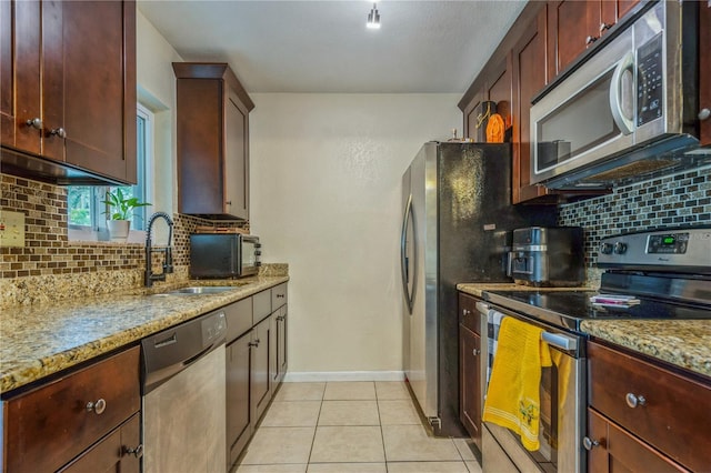 kitchen with tasteful backsplash, sink, light tile patterned flooring, light stone countertops, and stainless steel appliances