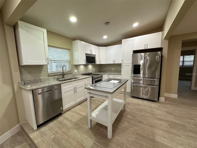 kitchen featuring stainless steel appliances, vaulted ceiling, white cabinets, light stone counters, and sink