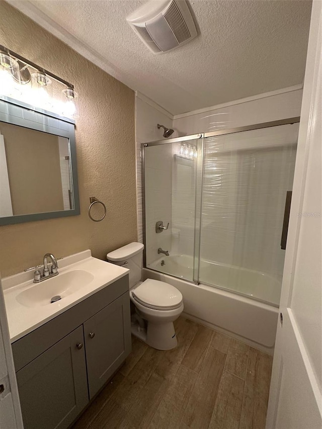 full bathroom featuring a textured ceiling, shower / bath combination with glass door, wood-type flooring, vanity, and toilet