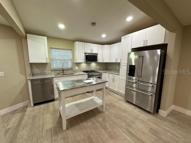 kitchen featuring light stone countertops, stainless steel appliances, white cabinetry, and sink