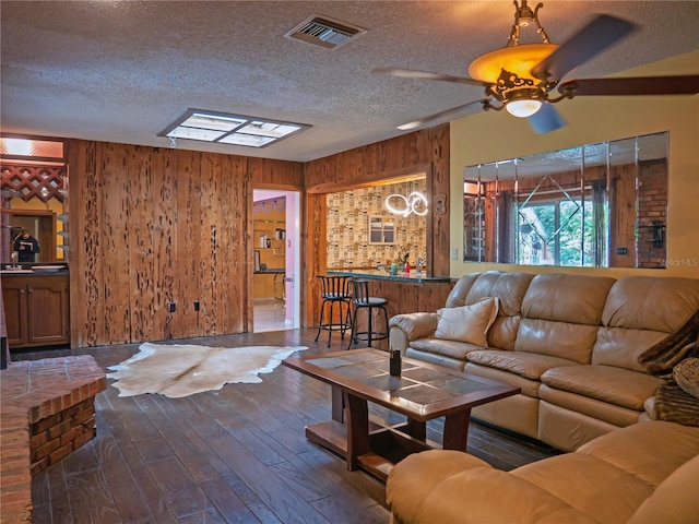 living room with wood walls, a textured ceiling, indoor bar, dark hardwood / wood-style floors, and ceiling fan