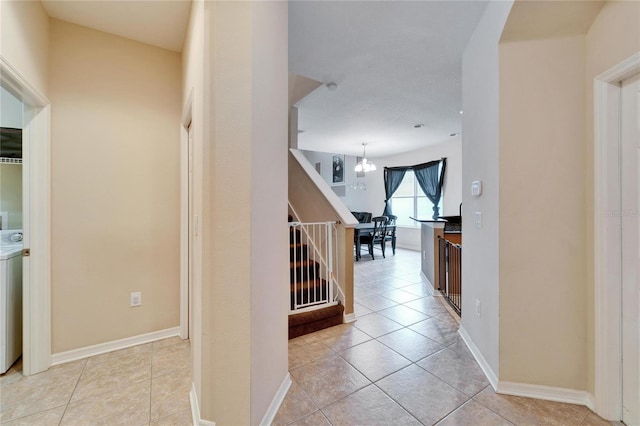 hall featuring light tile patterned floors, a chandelier, and independent washer and dryer