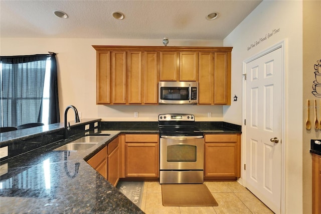 kitchen with light tile patterned floors, sink, appliances with stainless steel finishes, and dark stone countertops