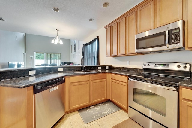 kitchen with stainless steel appliances, dark stone countertops, sink, a notable chandelier, and light tile patterned floors