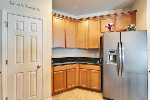 kitchen featuring stainless steel fridge with ice dispenser, light tile patterned floors, a textured ceiling, and dark stone counters