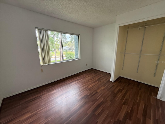 unfurnished bedroom with wood finished floors, a textured ceiling, a closet, and baseboards