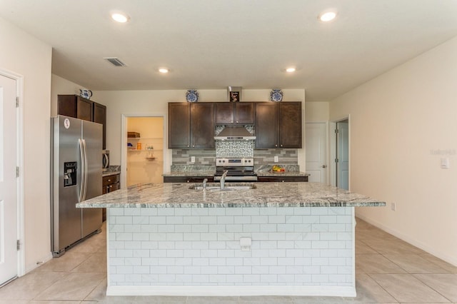 kitchen featuring appliances with stainless steel finishes, an island with sink, sink, light tile patterned floors, and dark brown cabinetry