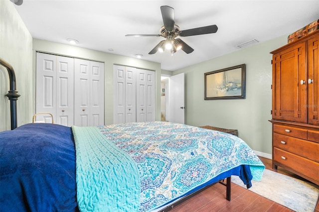 bedroom with ceiling fan, hardwood / wood-style floors, and multiple closets