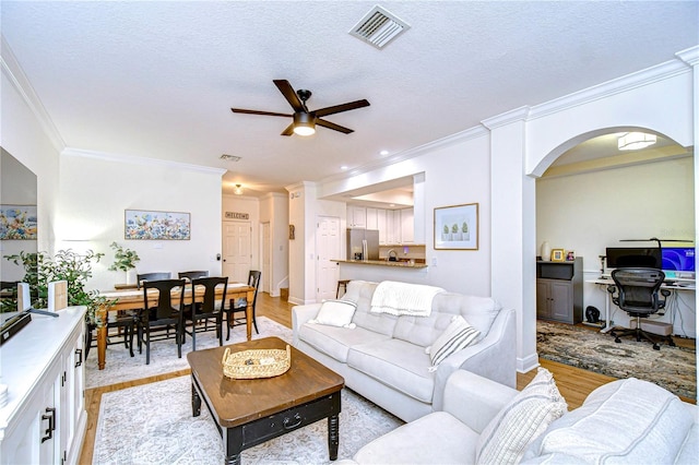 living room with ceiling fan, a textured ceiling, light hardwood / wood-style flooring, and crown molding