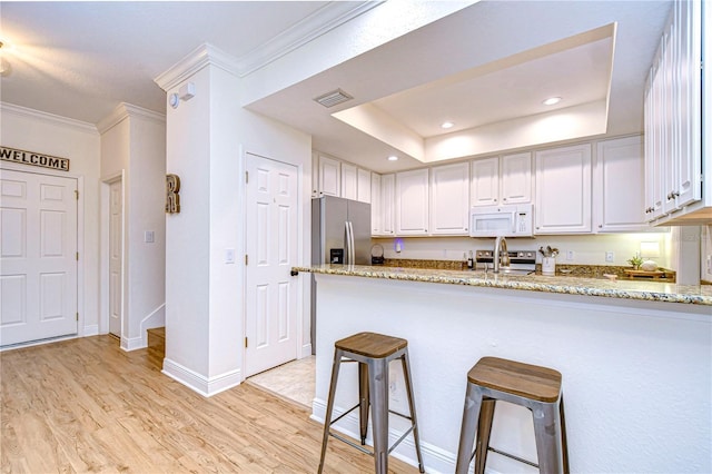 kitchen featuring crown molding, white cabinetry, light stone countertops, a breakfast bar area, and stainless steel appliances