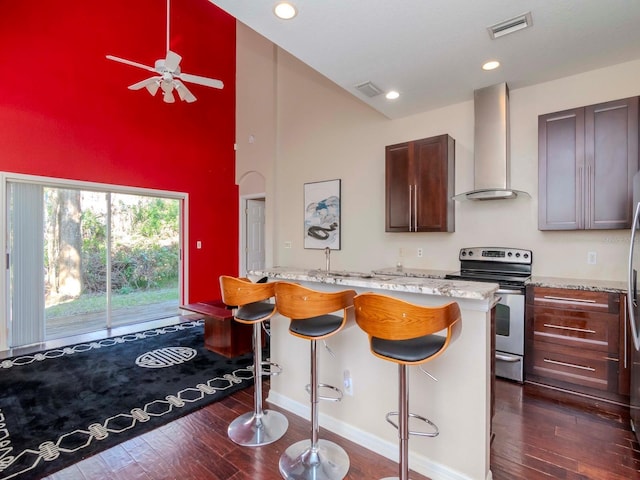 kitchen with stainless steel range with electric stovetop, high vaulted ceiling, a kitchen breakfast bar, dark hardwood / wood-style floors, and wall chimney exhaust hood