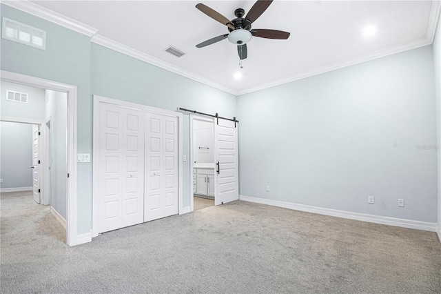 unfurnished bedroom with crown molding, connected bathroom, ceiling fan, and a barn door