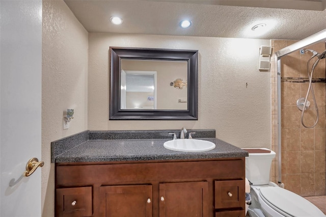 bathroom featuring a textured ceiling, toilet, a tile shower, and vanity