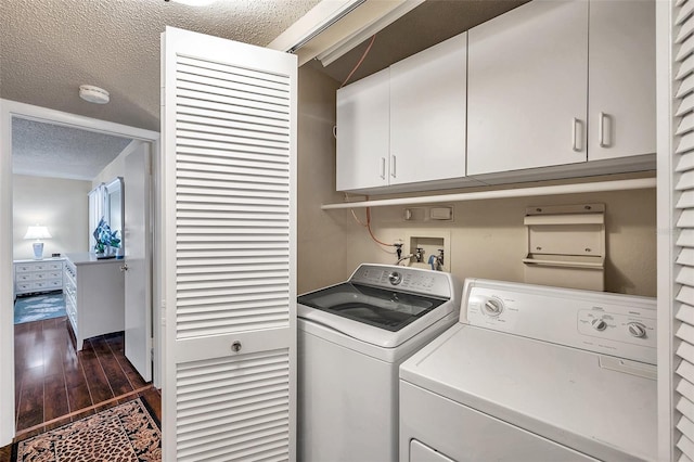 laundry area with a textured ceiling, separate washer and dryer, dark hardwood / wood-style floors, and cabinets