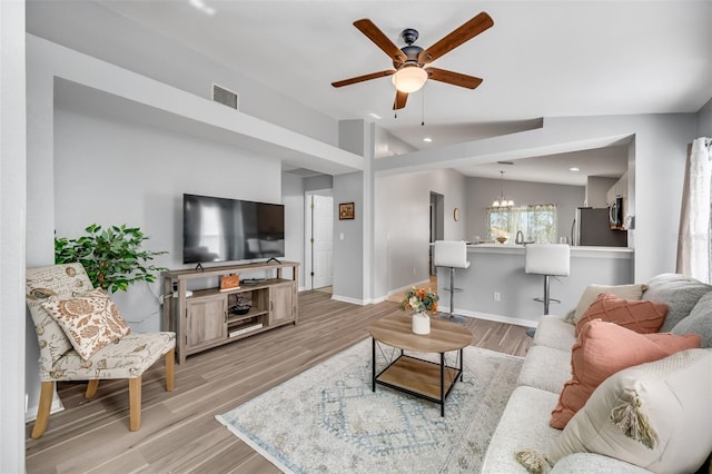 living room featuring lofted ceiling, ceiling fan with notable chandelier, and light hardwood / wood-style flooring