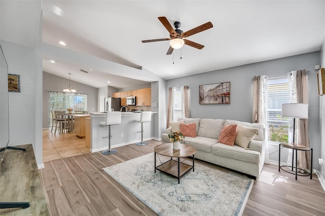 living room with lofted ceiling, ceiling fan with notable chandelier, and light hardwood / wood-style floors