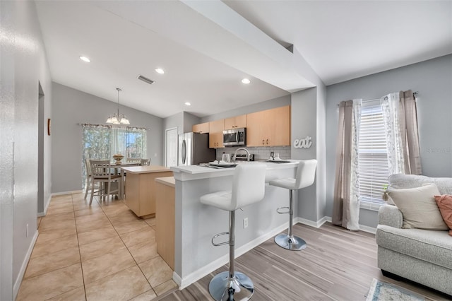 kitchen featuring a breakfast bar area, appliances with stainless steel finishes, light brown cabinets, decorative light fixtures, and lofted ceiling