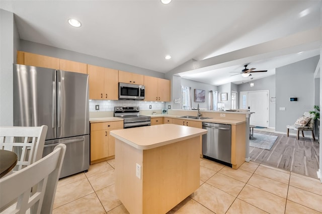 kitchen featuring light brown cabinetry, a center island, stainless steel appliances, and vaulted ceiling