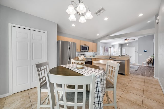 tiled dining space featuring vaulted ceiling, sink, and ceiling fan with notable chandelier