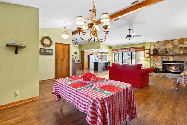 dining room featuring ceiling fan with notable chandelier, hardwood / wood-style flooring, a stone fireplace, and vaulted ceiling with beams