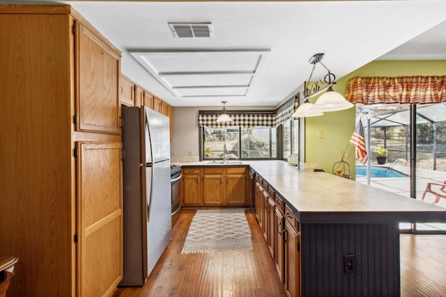 kitchen with light hardwood / wood-style floors, kitchen peninsula, sink, stainless steel refrigerator, and hanging light fixtures