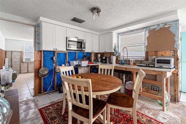 kitchen featuring sink, white cabinetry, light tile patterned floors, and a textured ceiling