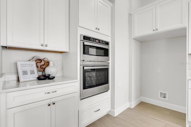 kitchen with stainless steel double oven, light wood-type flooring, and white cabinets