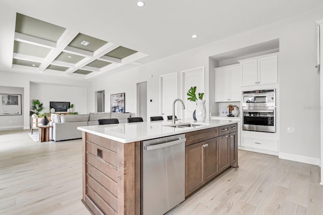 kitchen with coffered ceiling, light hardwood / wood-style flooring, appliances with stainless steel finishes, an island with sink, and white cabinets