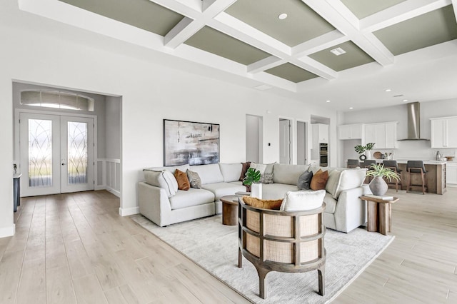 living room with coffered ceiling, a towering ceiling, french doors, and light wood-type flooring