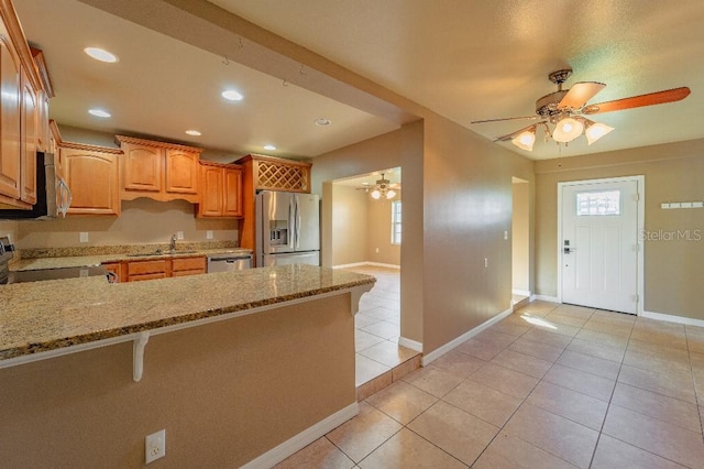 kitchen with kitchen peninsula, stainless steel appliances, light tile patterned flooring, light stone counters, and sink