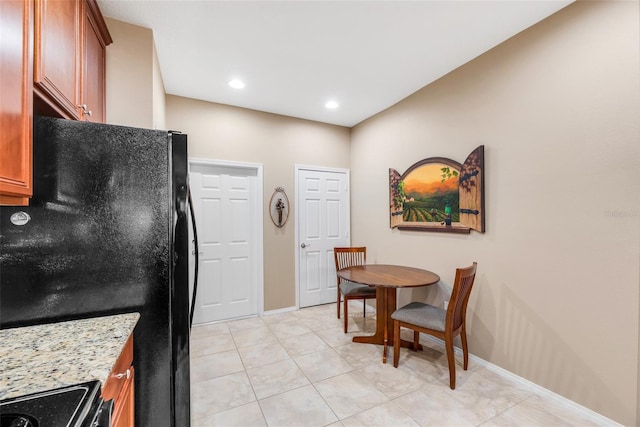 kitchen with light stone counters, light tile patterned floors, range, and black fridge