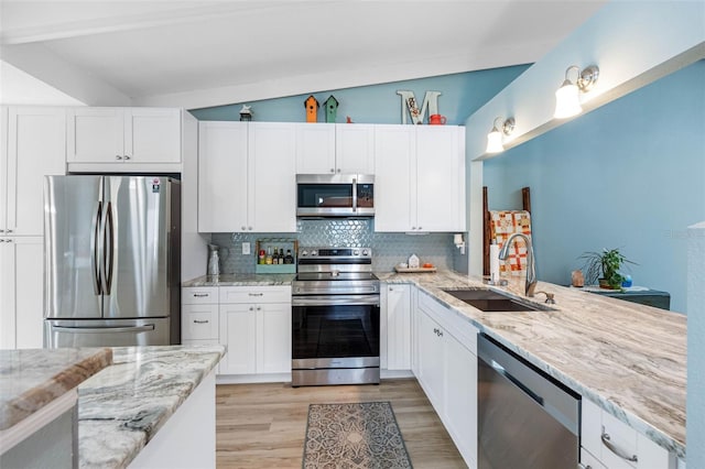 kitchen featuring backsplash, vaulted ceiling, sink, white cabinetry, and stainless steel appliances